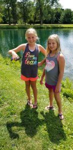 Two young girls standing by a lake holding a painted turtle