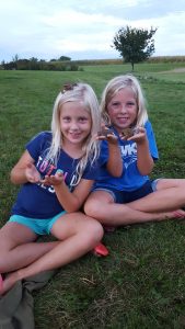 Two young girls sitting in the grass holding toads
