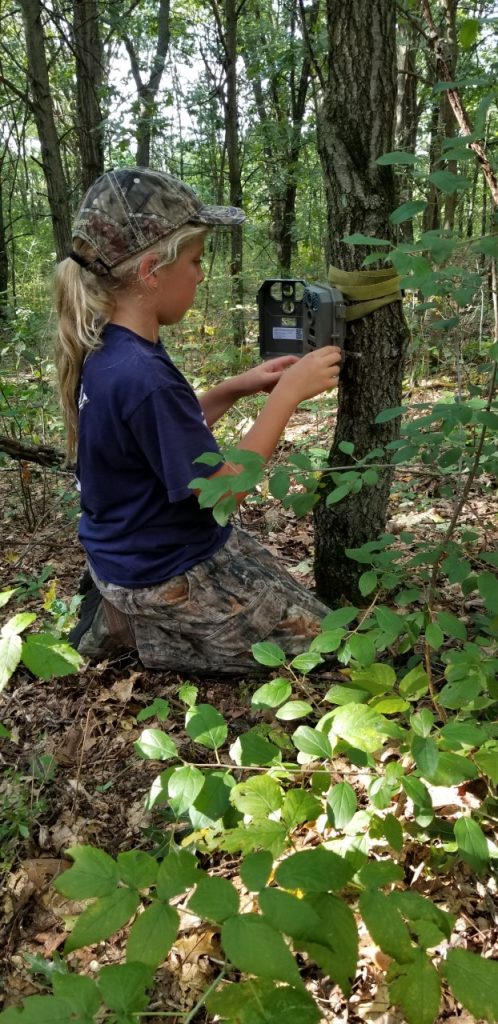 a girl setting up a trail camera in the woods