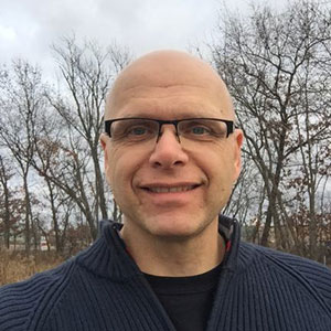 A bald man with glasses and a blue sweater