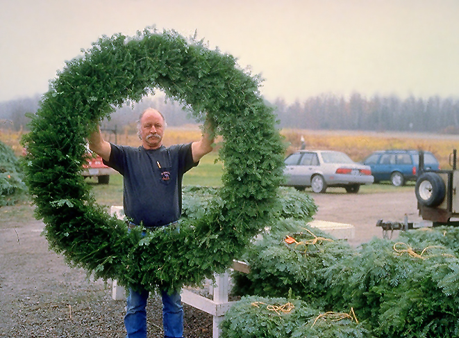 A man holds up a large balsam fir wreath