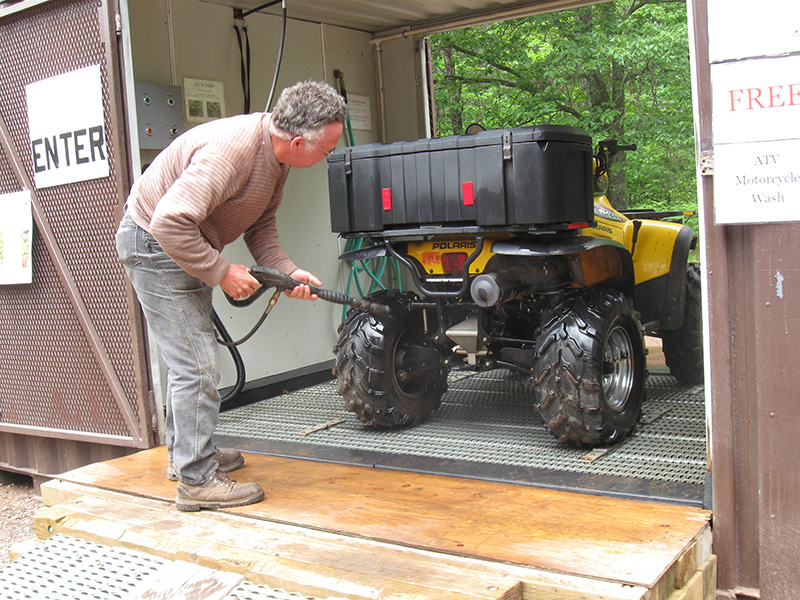 A man uses a hose to wash an ATV.