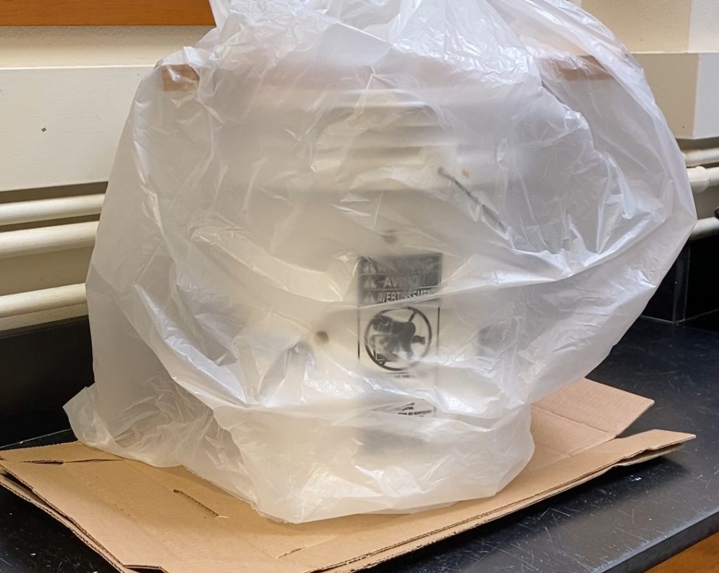 bucket sitting on cardboard and covered by transparent plastic bag