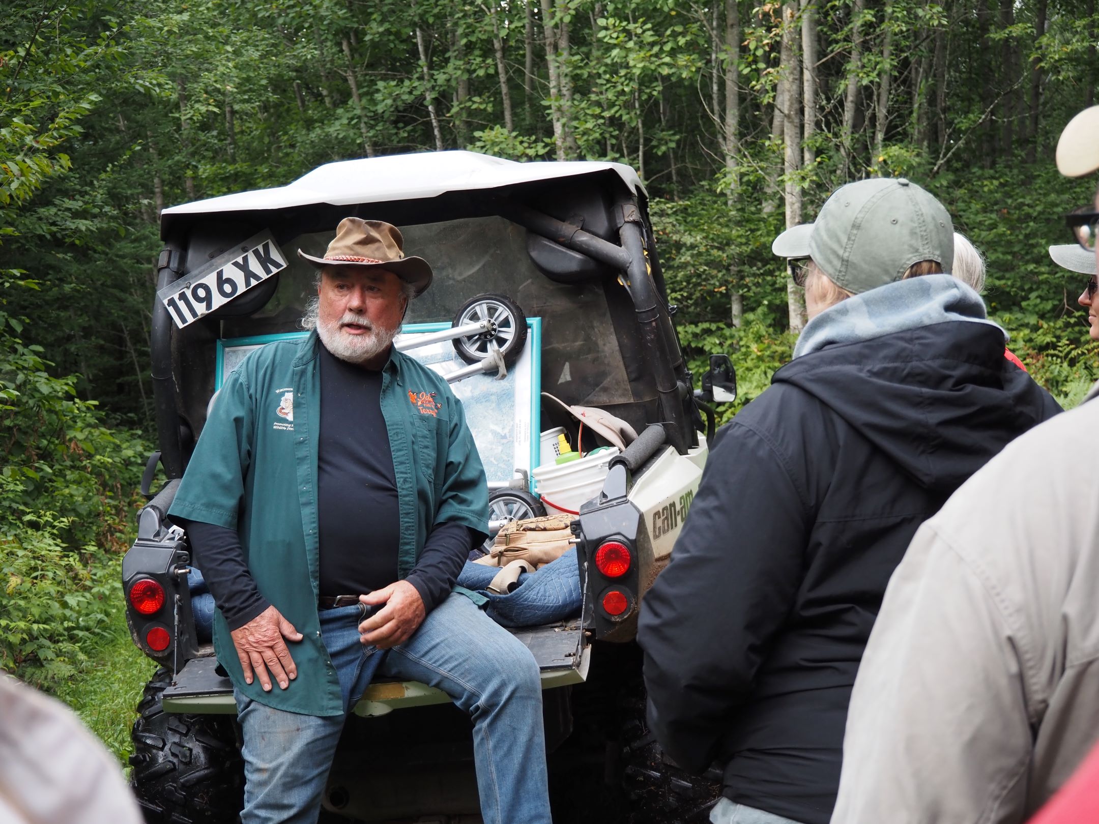 a man speaking to a crowd of people in a forest