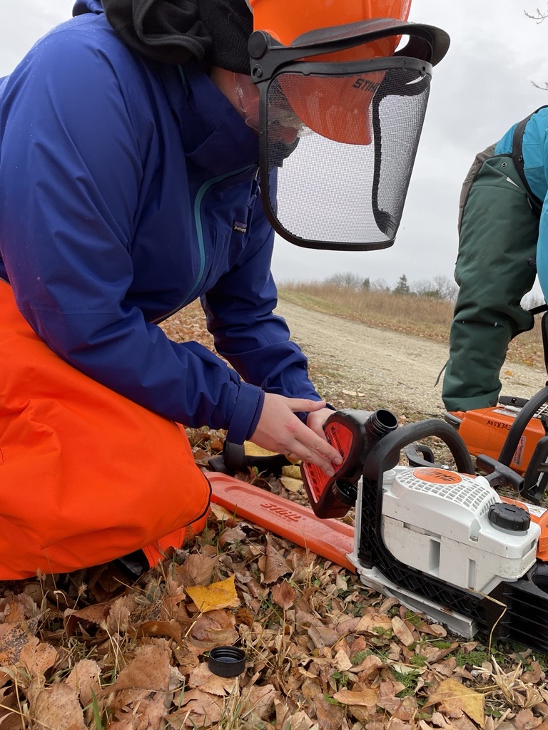 A person pours oil into a chainsaw