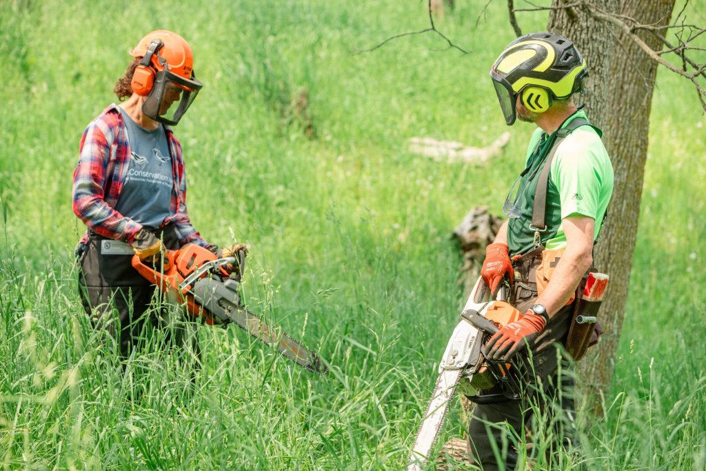 two people holding chainsaws and wearing protective gear