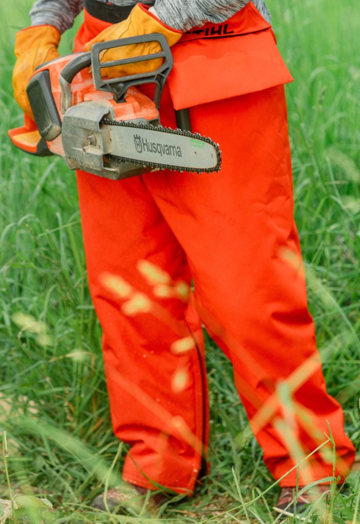 a person wearing chaps and gloves and holding a chainsaw