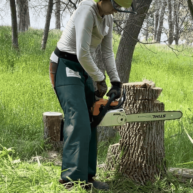 a person starting a chainsaw with the chainsaw held between their legs