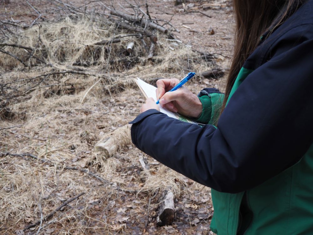 A person writing notes on a clipboard while standing outside