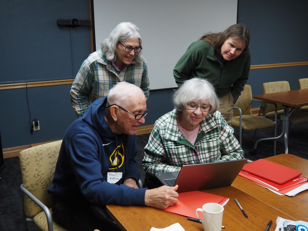 four people smiling and looking at a computer screen
