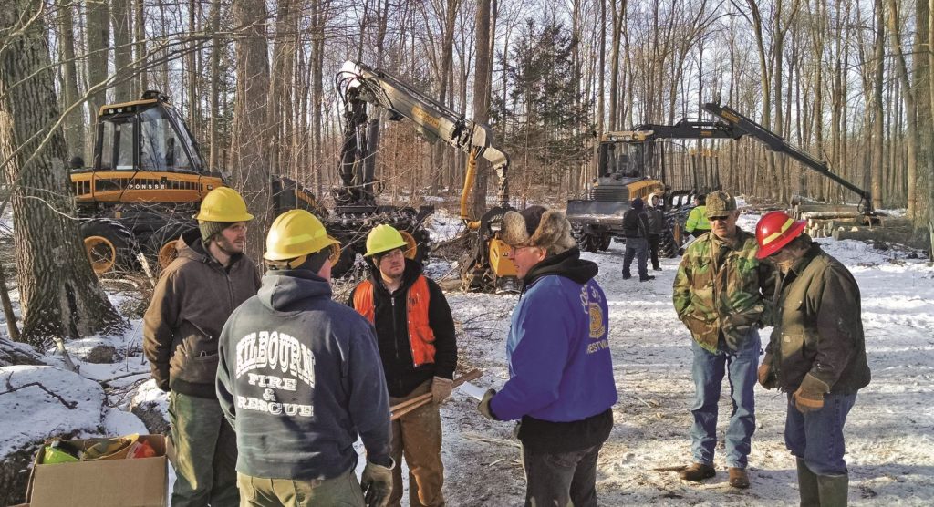 a group of people in hard hats with logging equipment in the background