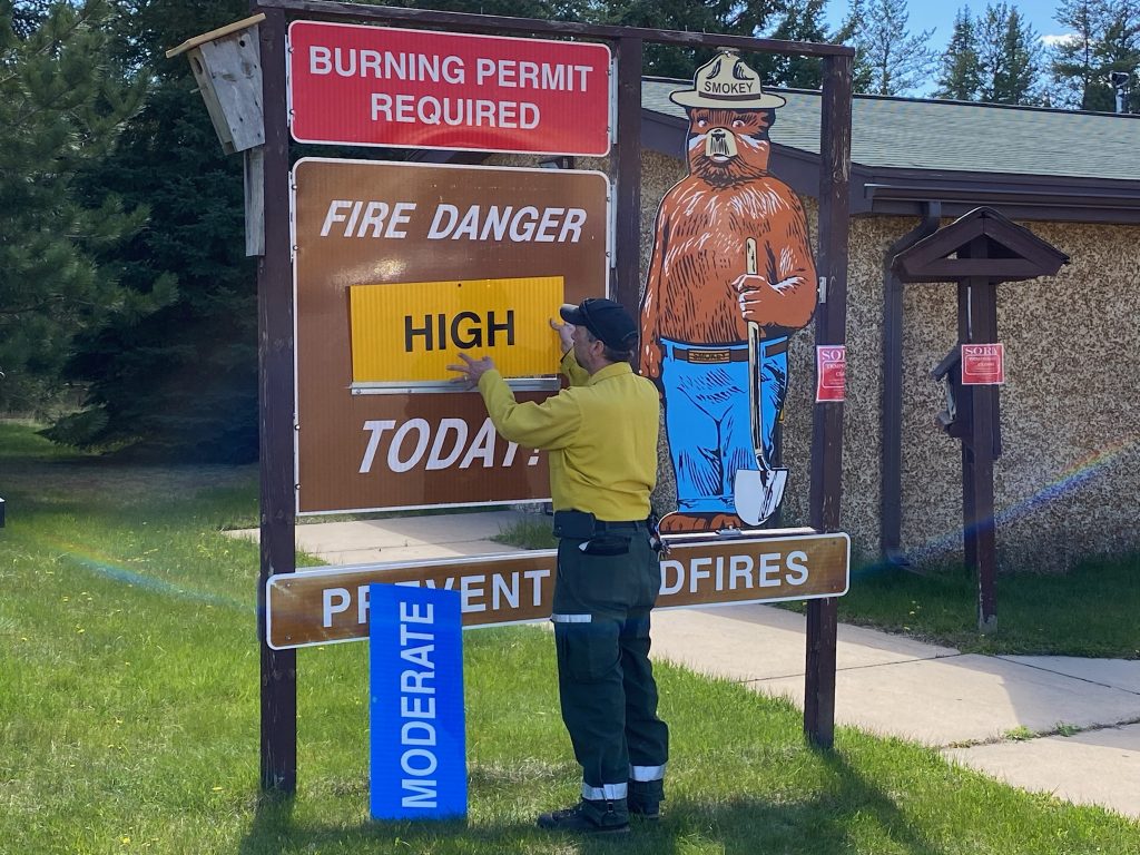 A person updates an outdoor fire danger sign to say "high" instead of "moderate"